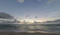 a picture of a beach with waves coming towards shore and clouds in the distance with a sunset in the background