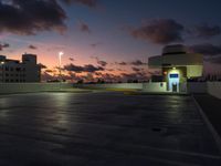 a parking lot with buildings on either side of it at dusk, and clouds and lights in the sky