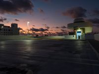 a parking lot with buildings on either side of it at dusk, and clouds and lights in the sky