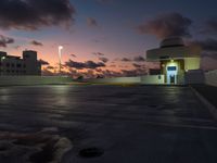 a parking lot with buildings on either side of it at dusk, and clouds and lights in the sky