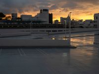 view from a roof over a parking lot under a cloudy sky at sunset with high rise buildings in the background