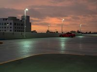 a red sports car is parked in an empty parking lot at dusk in the rain