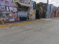 a person on a skateboard next to a graffiti covered street wall in the middle of an empty city