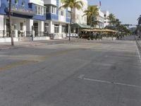 a view of the street from a sidewalk in front of an empty building, with palm trees along the street