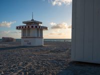 a life guard stand in the sand near the ocean as the sun goes down on a beach