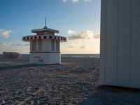 a life guard stand in the sand near the ocean as the sun goes down on a beach