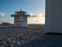 a life guard stand in the sand near the ocean as the sun goes down on a beach