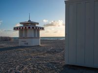 a life guard stand in the sand near the ocean as the sun goes down on a beach