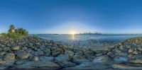 a view out to the water from behind rocks, which are scattered with trees and tall buildings in the distance