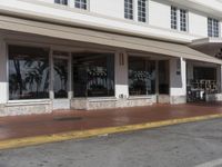 empty sidewalk outside office with open door and white building frontage and palm trees in window