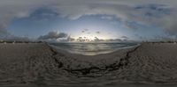 a sun reflecting off the ocean into a body of water with sand and clouds above