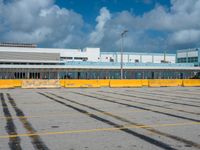 an empty parking lot filled with lots of buildings and trucks in the background of a cloudy blue sky