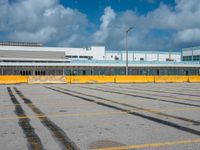 an empty parking lot filled with lots of buildings and trucks in the background of a cloudy blue sky