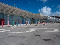 parking lot and building at an airport, with multiple colors painted on the pavement and columns, as well as a blue sky