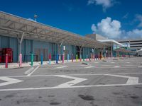 parking lot and building at an airport, with multiple colors painted on the pavement and columns, as well as a blue sky