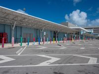 parking lot and building at an airport, with multiple colors painted on the pavement and columns, as well as a blue sky