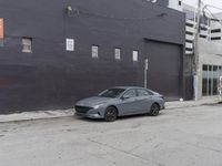 a silver car parked in front of a parking garage in front of the sidewalk and brick walls of an abandoned building