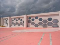 a white and grey wall with geometric designs on it on a red ground below the clouds