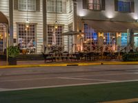 a building that has tables outside at night on a street corner, a red light is lit from a neon