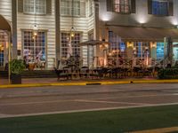 a building that has tables outside at night on a street corner, a red light is lit from a neon