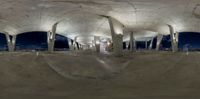 a skateboarder stands and looks at another skate board in an empty area with concrete pillars