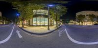 an intersection with a number of trees and buildings on the corner at night time, with no traffic