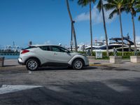 a car is parked in the lot by a dock with yachts and palm trees