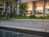 a person sitting on a skateboard near the pool with a building behind them in the background