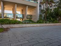 a man walking on the sidewalk in a modern style building setting at sunset, with green trees behind him