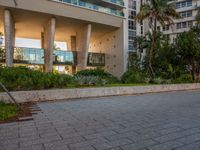 a man walking on the sidewalk in a modern style building setting at sunset, with green trees behind him