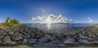 the ocean and rocks are all covered in white clouds and sunlight shining through it, the sky is a bright blue