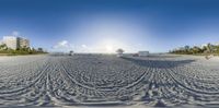 a beach with the sun behind a building in the distance and buildings on the sand