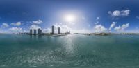 a wide shot of the sun rising over a body of water and city buildings in the distance