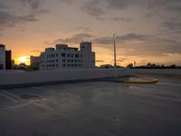 a parking lot with many parking spaces in the middle of it at sunset in front of large buildings and parking lights