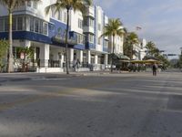 an empty city street with a white building and palm trees on both sides of the road