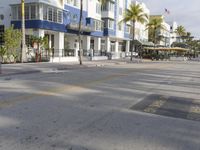 an empty city street with a white building and palm trees on both sides of the road