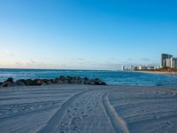 a beautiful beach with several footprints in the sand by the ocean and buildings behind the water