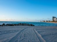 a beautiful beach with several footprints in the sand by the ocean and buildings behind the water