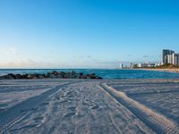 a beautiful beach with several footprints in the sand by the ocean and buildings behind the water