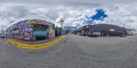 a man taking a selfie with a fish eye view of graffiti covered buildings in the background