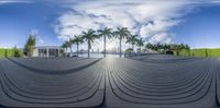 a panoramic view of a building with a circular walkway, palm trees, and a blue sky