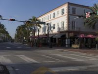 an intersection has white and tan colored buildings and palm trees in front of it for signs