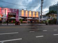 people outside a restaurant and the street is lit by some colorful lights, with palm trees