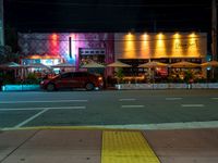 cars are parked outside an empty building that has colorful lighting at night and the colors are projected in multiple directions