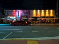 cars are parked outside an empty building that has colorful lighting at night and the colors are projected in multiple directions