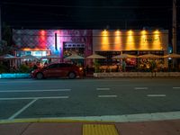 cars are parked outside an empty building that has colorful lighting at night and the colors are projected in multiple directions