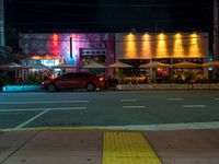 cars are parked outside an empty building that has colorful lighting at night and the colors are projected in multiple directions