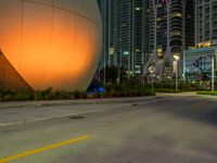 a big white sphere that is in the middle of a street at night, with skyscrapers in the background