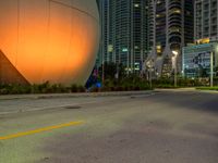 a big white sphere that is in the middle of a street at night, with skyscrapers in the background