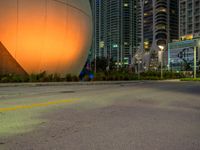 a big white sphere that is in the middle of a street at night, with skyscrapers in the background